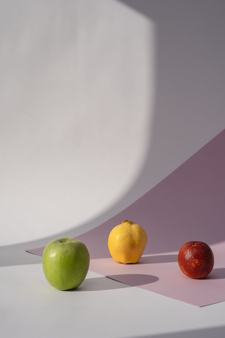 A modern still life composition featuring an apple, quince, and orange against a minimalistic pastel background.