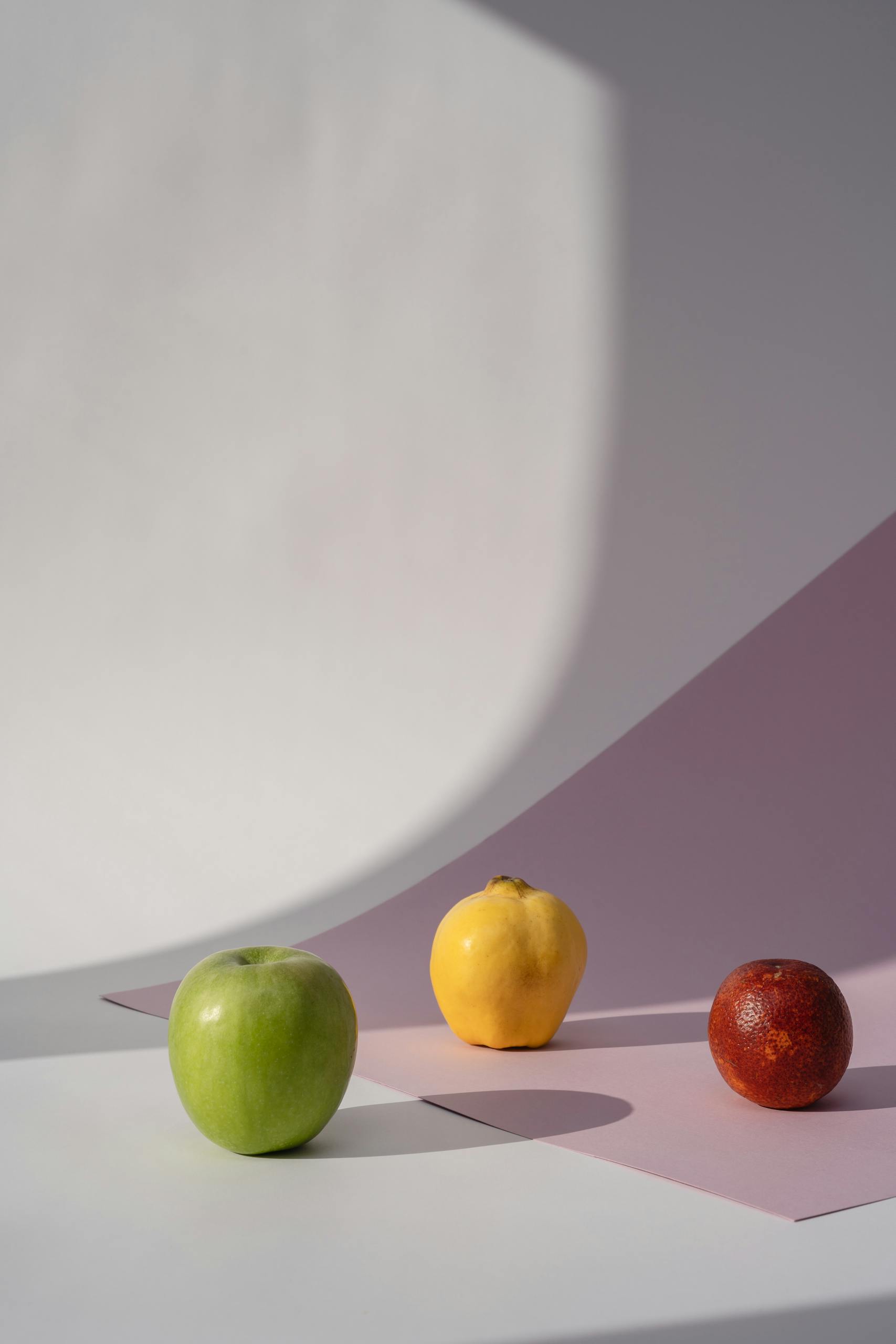 A modern still life composition featuring an apple, quince, and orange against a minimalistic pastel background.